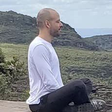 Ramon F. Bertasi sentado sobre uma pedra, diante de uma paisagem de montanhas